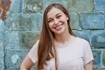 Smiling young woman in pink t-shirt on gray wall background