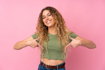 Young blonde woman with curly hair isolated on pink background proud and self-satisfied