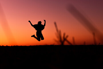 Obraz na płótnie Canvas A silhouette of a happy woman who is jumping in front of a sunset