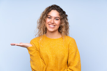 Young blonde woman with curly hair isolated on blue background holding copyspace imaginary on the palm to insert an ad