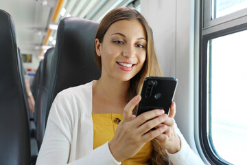 Smiling Brazilian businesswoman using smartphone social media app while commuting to work in train. Woman sitting in transport enjoying travel.