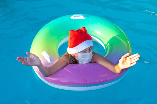 Little girl in santa claus hat and medical mask swims alone in the pool. New Year 2021 during the pandemic. The concept of the second wave of coronavirus in the world