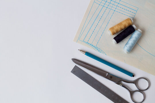 needlework. sewing thread, pencil, ruler, scissors and patterns on a white table of a fashion designer. top view. copy space. offices tools on white background