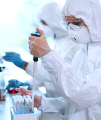 Scientists in protection suits and masks working in research lab using laboratory equipment:...