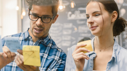Male Young Developer and Female Manager Brainstorming, They Have Discussion and Use Glass Board and Sticky Papers to Conceptualize Their New Plan. Creative People in Stylish Office Environment.