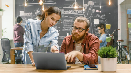Female Designers Talks Male Developer About Ongoing Project while He Works on a Laptop. In the...