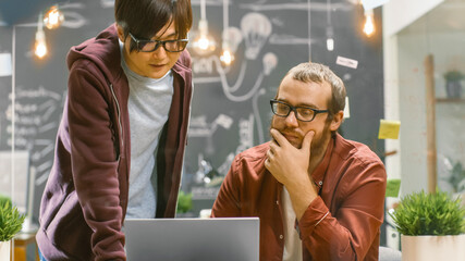 Two Creative Designers Looking at the Laptop and Trying to Find Problem Solution. In the Background Modern Stylish Loft Office.