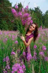Smiling young woman holding the bouquet of pink flowers. Pink Ivan Tea or blooming Sally in the field