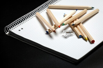 White notebook , color pencils and pencil sharpener on a table against black background. Preparing for a school. Back to school.