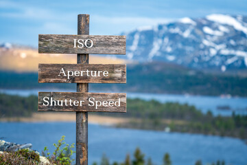 iso, aperture and shutter speed text on wooden signpost outdoors in landscape scenery during blue hour and sunset.