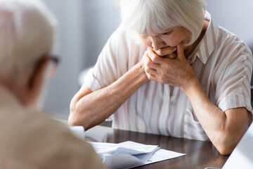 Selective focus of sad elderly woman looking at documents near husband at home