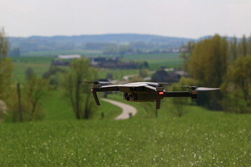 A generic drone hoovering over a beautiful meadow, with a curvy road in a landscape on the background. The camera is under the rotating blades. Flying a drone is the newest hype in aviation technology