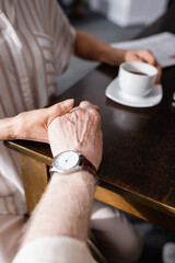 Cropped view of senior couple holding hands while drinking coffee at home