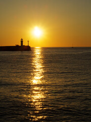 Fototapeta na wymiar Sunrise over a lighthouse in the sea
