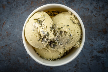 Pistachio ice cream balls with nuts in a paper white glass on a gray stone background