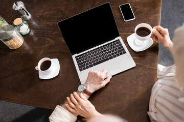 Overhead view of senior woman touching husband using laptop near coffee and smartphone on table