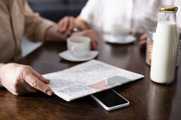 Cropped view of senior man holding newspaper near wife during breakfast in kitchen