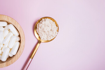 White powder in a spoon and pills on pink background.