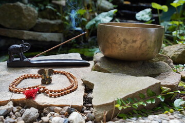 Bronze Tibetan singing bowl with wooden Mala and ganesha deity in front of the bowl.