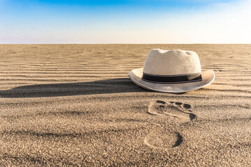 Fototapeta na wymiar Footprint and hat on the sand. Summer and holiday concept with sandy beach. 