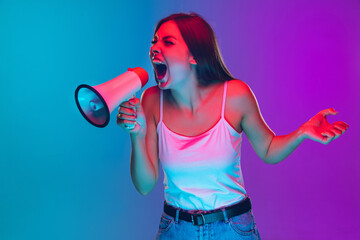 Shouting with megaphone. Caucasian young woman's portrait on gradient background in neon light. Beautiful female model. Concept of human emotions, facial expression, sales, ad. Copyspace.