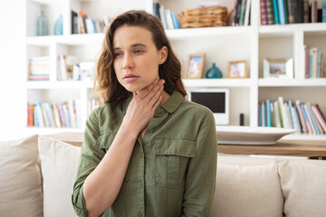 Woman with sore throat holding her neck at home