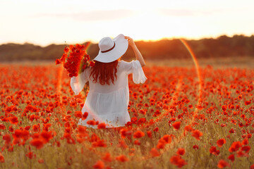 Beautiful redhead woman with bouquet of poppies in hat on green field