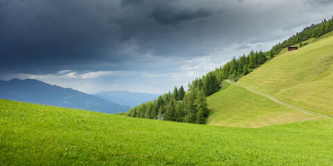Panorama einer Almlandschaft mit Bergwiese und Gewitterwolken