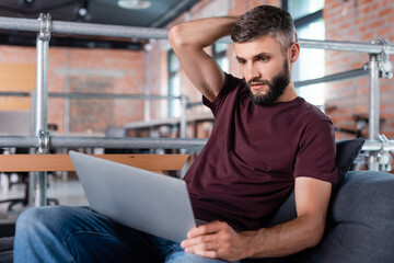 handsome businessman sitting on sofa and looking at laptop in office