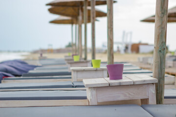 Obraz na płótnie Canvas Focus on the cup on the wooden table next to the sun lounger on the beach bar. The beach is empty and there is no one.