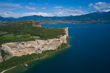Lake Garda, Italy. Aerial view of punta sasso, rocca di manerba in the background mountains, san biagio island cumulus clouds at high altitude
