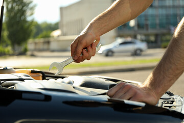 A man holds a wrench over a car engine. Car inspection