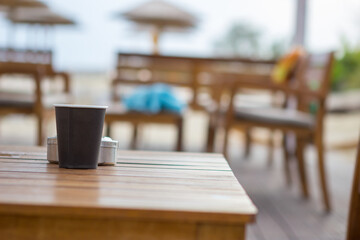 Focus on the black paper coffee cup on the table in the beach cafe. The cafe is empty and there are no people. copy space.