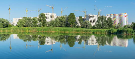 Beautiful summer landscape in Zhuravlevsky Hydropark with a view to the construction of new colored houses and construction cranes with reflection in the Kharkov river