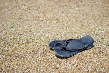 Fototapeta na wymiar Selective focus on old slippers. The slippers are on the yellow sand on the beach and it is a beautiful sunny day. Copy space.