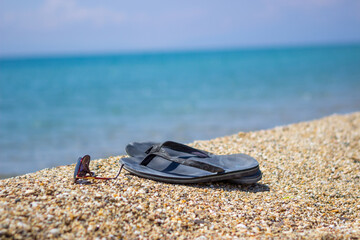 Selective focus on old slippers. Next are sunglasses. They are located on the yellow sand on the beach and it is a beautiful sunny day. Copy space.