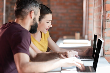 selective focus of happy businesswoman and businessman using laptops in office