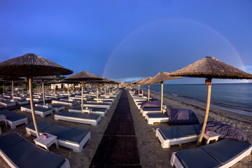 The dark blue sky is above the beach by the sea. It was as if there was a storm, and it turned out to be a rainbow. The beach is empty and there are no people.