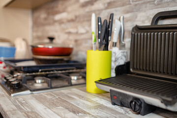 An electric grill, a set of knives and pans stand on the new wooden countertop