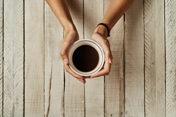 Women's hands with a coffee cup on a wooden table.