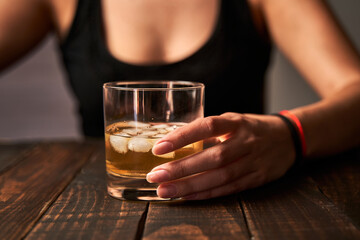 Drunk woman's hand holding a glass of alcohol. Concept of alcoholism and addictions.
