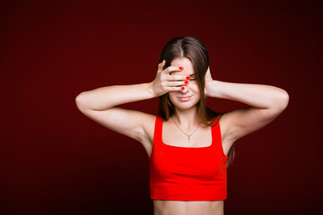 Portrait of a young girl who covered her ears and eyes with her hands due to severe migraine and noise on a red background.