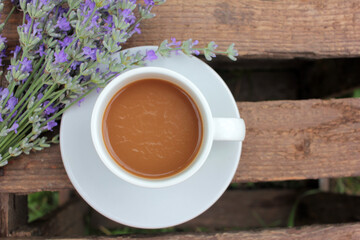Cup of coffee with milk or cappuccino and lavender flowers on wooden board in summer garden. Enjoying morning coffee. Top view, copy space. Selective focus
