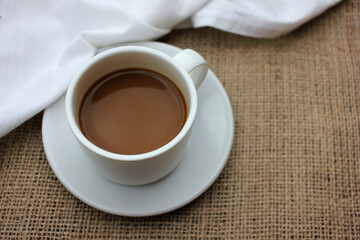 Cup of coffee with milk or cappuccino on burlap fabric texture with copy space. Enjoying summer morning coffee. Top view. Selective focus