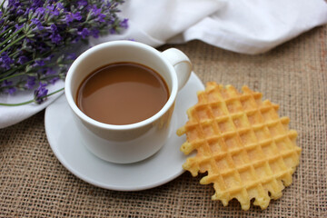 Cup of coffee with lavender flowers and waffle on burlap texture. Top view. Selective focus
