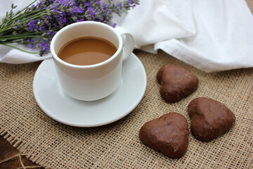 Cup of coffee with lavender flowers and chocolate heart shaped cookies on burlap texture. Top view