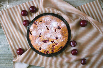 Delicious plum cake sprinkled with powdered sugar lies on a beautiful kitchen towel with ripe plums
