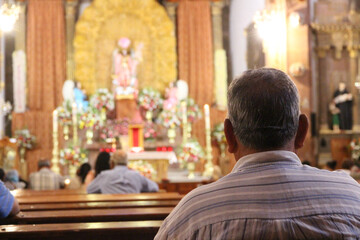 The back of an anonymous, elderly man, sitting in a nicely decorated Mexican church. A ceremony is...
