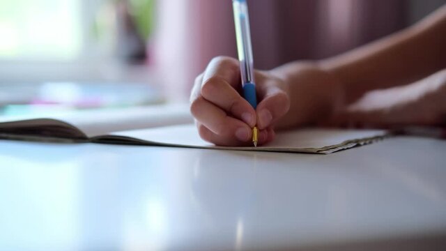 Close up of girls hands write on a sheet of paper. Writing an essay or letters. A schoolboy writes in a notebook. He does lessons in a medical mask. Doing homework.