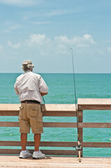 Back view, medium distance of a senior male fishing off a wood pier in the tropical waters of the gulf of Mexico on a sunny day